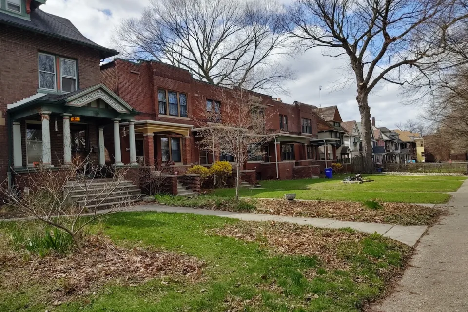 Row of older brick houses in Detroit with front porches and front lawns.